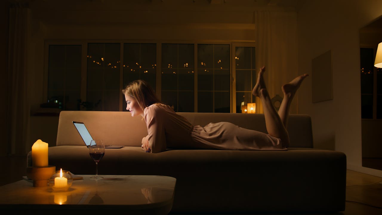 gallery-02 Caucasian woman smiling and relaxing on a sofa with a laptop at night.